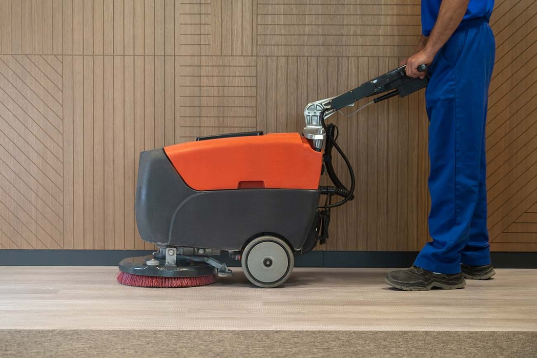 An employee using an industrial floor cleaner or scrubber in front of a wood-paneled wall.